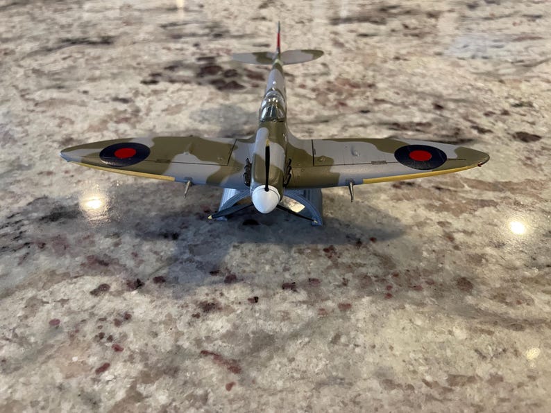 May include: A detailed model of a British Supermarine Spitfire fighter plane with a camouflage paint scheme of green, brown, and gray. The plane has red, white, and blue roundels on the wings.