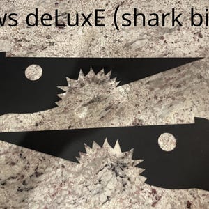 Op de afbeelding: Twee zwarte, uitgesneden haaienvinvormen met gekartelde randen. De tekst "Jaws deLuxE (shark bite)" staat bovenaan de afbeelding.