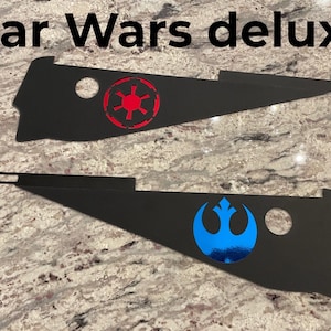 May include: Two black metal Star Wars themed signs. The top sign features the Imperial symbol in red. The bottom sign features the Rebel Alliance symbol in blue.