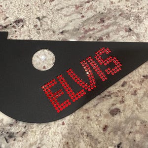 May include: Black triangular sign with the word "ELVIS" spelled out in red rhinestones.
