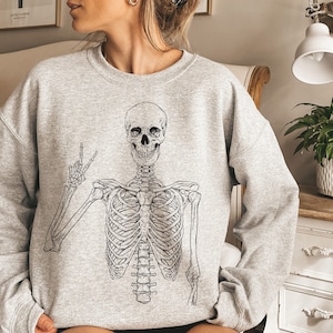 May include: A gray sweatshirt with a black and white skeleton graphic wearing a peace sign. The skeleton is in a relaxed pose with its arms outstretched.