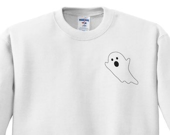 May include: A white crewneck sweatshirt featuring a small, black-outlined ghost graphic on the upper left chest. The ghost has two circular eyes and an oval-shaped mouth, creating a simple, minimalist design on the plain white fabric.