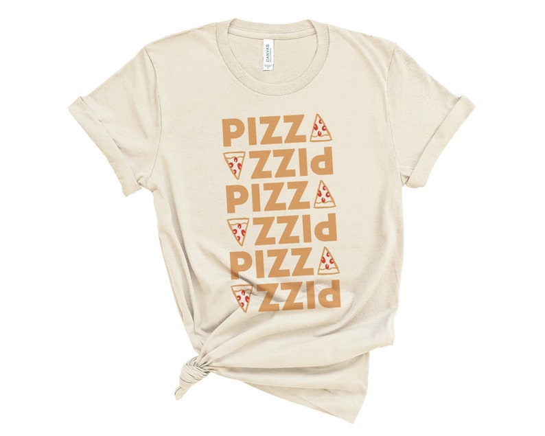 May include: Cream-colored t-shirt with the word "PIZZA" repeated vertically in a brown font. Each instance of the word "PIZZA" has a pizza slice graphic next to it. The shirt is knotted at the bottom.