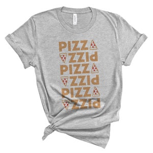 May include: A heather gray t-shirt with the word "PIZZA" repeated vertically five times in a brown font. Each instance of the word has a pizza slice graphic. The shirt is knotted at the bottom.
