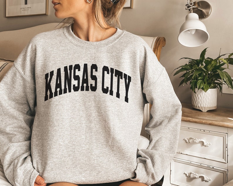 May include: A gray sweatshirt with the text "KANSAS CITY" printed in black on the front.