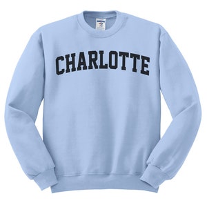 May include: A light blue sweatshirt with the word "CHARLOTTE" printed across the chest in black, arched lettering. The long-sleeved crew neck top is made of a soft material.