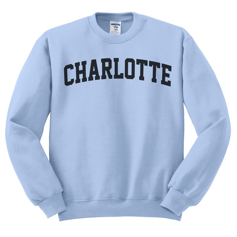 May include: A light blue sweatshirt with the word "CHARLOTTE" printed across the chest in black, arched lettering. The long-sleeved crew neck top is made of a soft material.