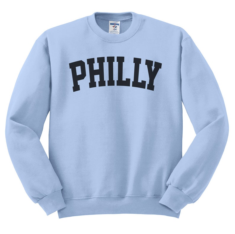 Puede incluir: Una sudadera de color azul claro con la palabra "PHILLY" impresa en negro en la parte delantera.