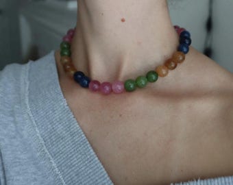 May include: A multi-colored beaded necklace with a variety of colors including pink, green, blue, and orange. The necklace is made of round beads and is worn around the neck. The necklace is a piece of jewelry.