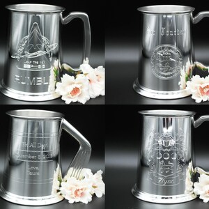 May include: Four silver pewter tankards with different engraved designs. The tankards have a rounded body and a handle. The designs include a crest, a ship, a crest with a dog, and a crest with a bird.
