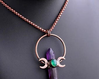 May include: A copper necklace with a pendant featuring a purple amethyst crystal point, a green gemstone, and three crescent moons.
