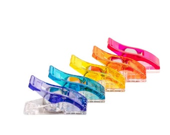 May include: A set of six colorful plastic fabric clips in a rainbow gradient. The clips are arranged in a row, with the red clip at the top and the blue clip at the bottom. The clips are used for holding fabric together while sewing.