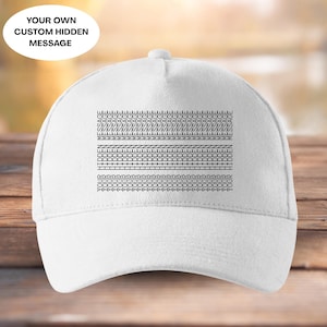 May include: White baseball cap with a curved peak. The cap displays a series of black geometric patterns across the front. The text "YOUR OWN CUSTOM HIDDEN MESSAGE" is printed on the top left of the cap.