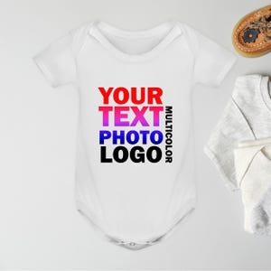 Puede incluir: Body de bebé blanco con el texto "YOUR TEXT PHOTO LOGO MULTICOLOR" en rojo, morado, azul y negro. El body es de manga corta. Un par de zapatos de bebé y un body doblado están en el fondo.