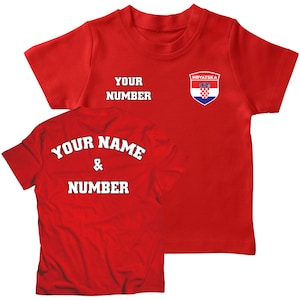 K&ouml;nnte beinhalten: Rotes T-Shirt mit einem wei&szlig;en kroatischen Wappen auf der Vorderseite und dem Text "YOUR NUMBER" und "HRVATSKA". Die R&uuml;ckseite des Shirts tr&auml;gt den Text "YOUR NAME & NUMBER" in Wei&szlig;.