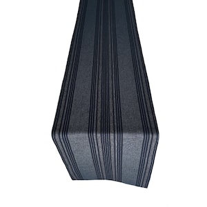 May include: A navy blue table runner with vertical stripes in a lighter shade of blue and a thin, neutral stripe. The runner is made of a textured fabric and is displayed against a white background. This home decor item is suitable for a dining table.