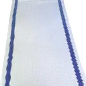 May include: White table runner with navy blue stripes on either side. The fabric has a textured appearance. The stripes feature a subtle herringbone design. The runner is displayed against a white backdrop. The runner is suitable for a dining table.