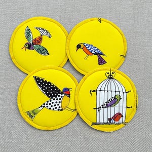 ファンキーなコースター セット - 黄色の生地に描かれた気まぐれなフォーク アートの鳥。鳥好きの方への楽しいギフト。
