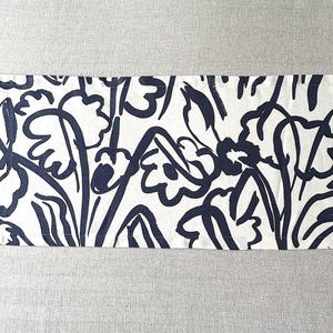 May include: A rectangular fabric runner featuring a bold, dark navy blue hand-drawn floral pattern printed on a crisp white background. The design consists of abstract, thick-lined flower and leaf motifs arranged in a continuous, repeating layout.