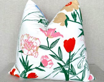 May include: A square throw pillow with a white background featuring a colorful floral print. The design includes pink peonies, bright red tulips, and beige blossoms, all connected by dark green stems and leaves in a hand-drawn style.