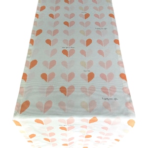 May include: White table runner with a repeating pattern of pink and orange hearts. The words "once upon a time", "two love", and "happily ever after" are printed on the runner.