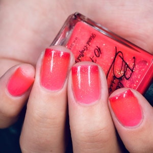 May include: Close-up of four fingernails with a pink and orange gradient nail polish. The polish has a shimmery finish. A bottle of nail polish is visible in the background. The bottle label reads "To-Die-For" and "Blood-Coated".
