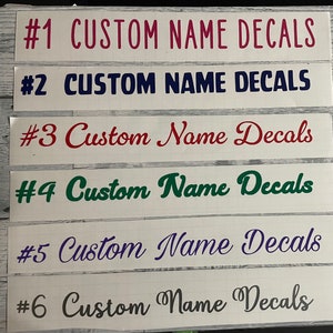 Può includere: Sei decalcomanie personalizzate con la scritta "Custom Name Decals" in vari colori e caratteri. I colori includono rosa, blu, rosso, verde, viola e grigio. Le decalcomanie sono numerate da uno a sei.