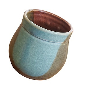 May include: A rounded ceramic cup featuring a smooth, light blue glazed band around the upper section, contrasting with a textured, earthy brown base. The interior of the cup is finished in a deep, reddish-brown glaze, creating a distinct color palette.