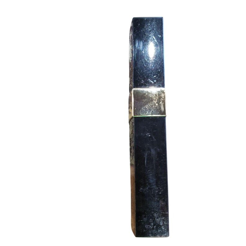 Puede incluir: Un envase de producto cosm&eacute;tico rectangular negro con una banda dorada. El envase tiene una superficie brillante y reflectante. El producto parece ser un l&aacute;piz labial o un art&iacute;culo de belleza similar.