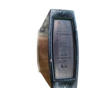 Puede incluir: Un frasco de perfume rectangular negro con el texto "CHANEL INC" y "N&deg;5" impreso en la parte delantera. El frasco contiene 41 ml de perfume. El frasco tiene un acabado oscuro y mate.