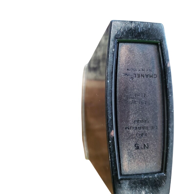 Puede incluir: Un frasco de perfume rectangular negro con el texto "CHANEL INC" y "N&deg;5" impreso en la parte delantera. El frasco contiene 41 ml de perfume. El frasco tiene un acabado oscuro y mate.
