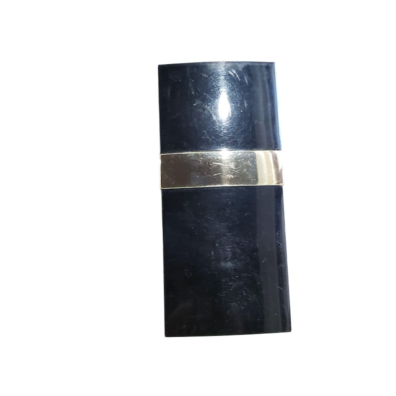 Puede incluir: Un tubo de l&aacute;piz labial negro con una banda plateada alrededor del centro. El envase del l&aacute;piz labial es rectangular y tiene un acabado brillante. El producto est&aacute; sobre un fondo blanco.