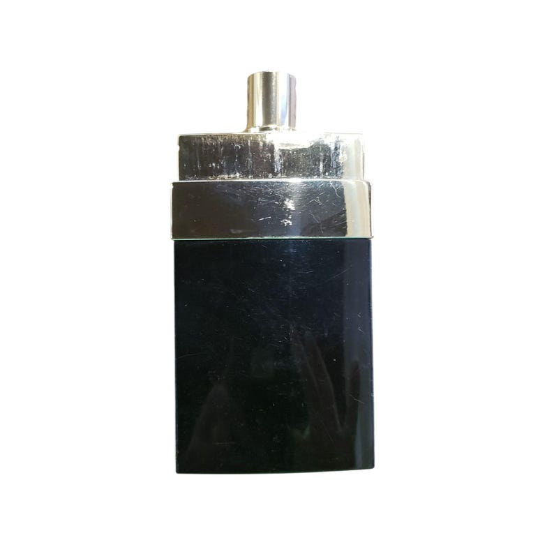 Puede incluir: Un frasco de perfume negro rectangular con tapa y ribete plateados. El frasco tiene un dise&ntilde;o elegante y minimalista, con una parte superior rectangular plateada y una tapa cil&iacute;ndrica plateada.