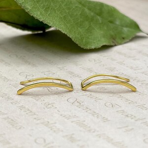 May include: A pair of gold ear cuffs. The ear cuffs are made of a thin, curved wire that is bent into a U-shape. The ear cuffs are designed to be worn on the upper part of the ear, just above the cartilage.