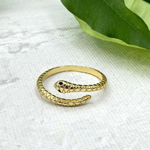 Peut inclure: Une bague serpent dorée avec un motif texturé en forme d'écailles. La tête du serpent présente un petit œil en pierre noire. La bague s'enroule, créant un accessoire unique et élégant. C'est un bijou.