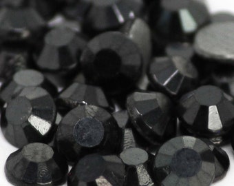 May include: A close-up of a pile of black rhinestones. The rhinestones are faceted and have a shiny finish.