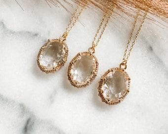 May include: Three gold necklaces with clear oval-shaped crystal pendants. The pendants have a detailed gold border.