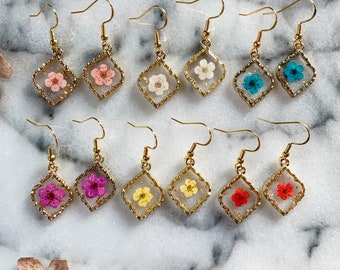 May include: A set of 10 pairs of gold earrings with different colored pressed flowers inside each diamond-shaped resin pendant.