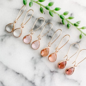 May include: A set of eight gold teardrop earrings with clear, pink, and rose-colored glass stones.