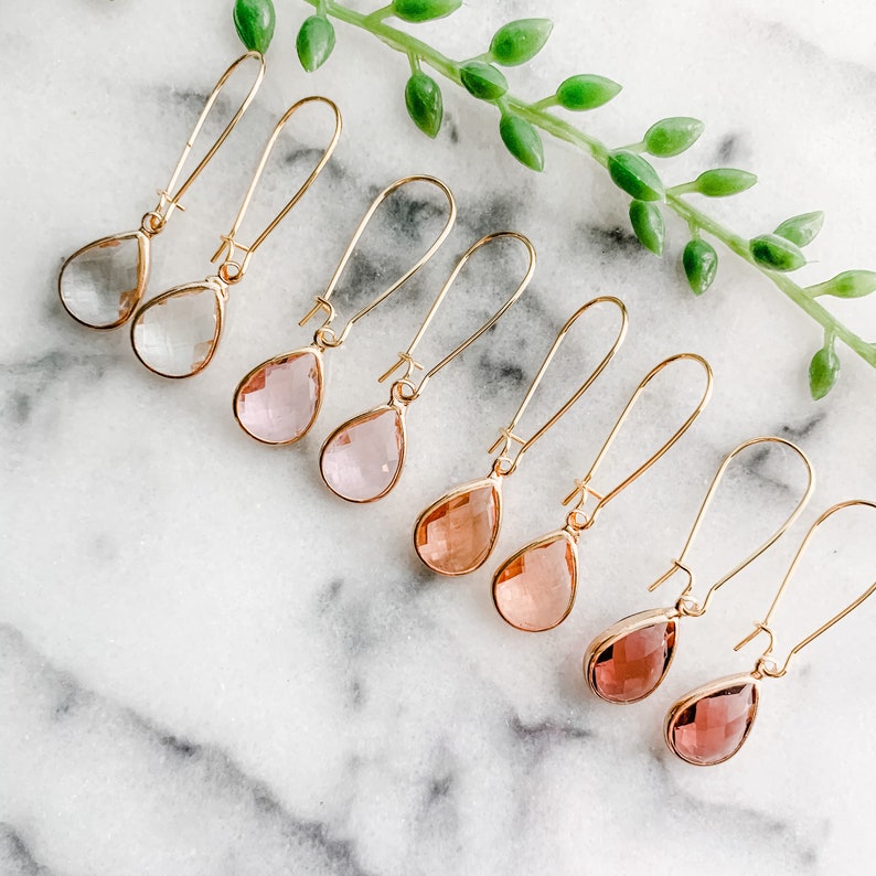May include: A set of eight gold teardrop earrings with clear, pink, and rose-colored glass stones.