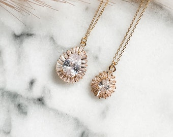 May include: Two gold necklaces with pear-shaped crystal pendants. The larger pendant has a larger crystal and a more elaborate setting.