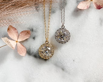 May include: Two silver and gold necklaces with a large round pendant featuring a clear crystal surrounded by smaller crystals.