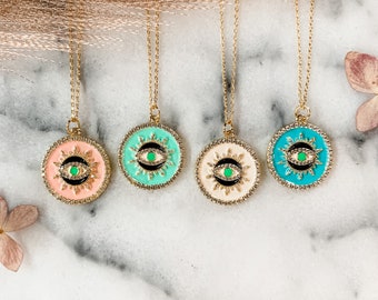May include: Four gold necklaces with a round pendant featuring an evil eye design. The pendants are in different colors: pink, turquoise, cream, and blue.