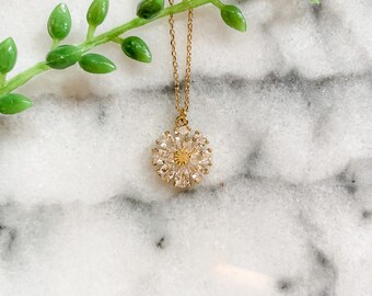 May include: A gold chain necklace with a flower-shaped pendant made of clear cubic zirconia stones.