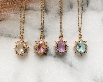 May include: Four gold necklaces with oval-shaped gemstone pendants. The pendants are surrounded by a halo of smaller stones. The gemstones are clear, pink, light purple, and light blue.