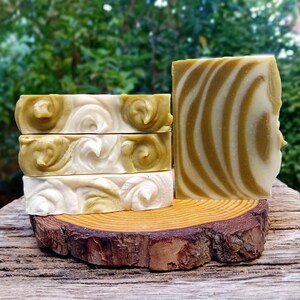 Puede incluir: Cuatro barras de jab&oacute;n artesanal con un dise&ntilde;o de remolino en tonos verdes y blancos. El jab&oacute;n se muestra en una rodaja de madera.