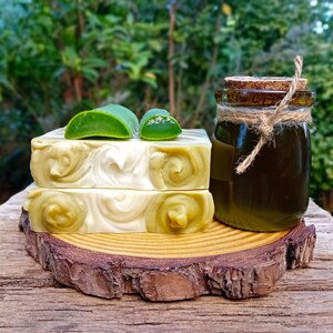 Puede incluir: Dos barras de jab&oacute;n de espiral verde y blanco sobre una rodaja de madera con un peque&ntilde;o frasco de vidrio de l&iacute;quido verde y una hoja de aloe vera verde encima del jab&oacute;n.