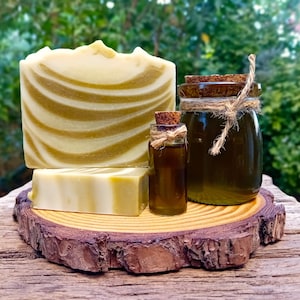 Puede incluir: Dos barras de jab&oacute;n de espiral verde y blanco y dos botellas de vidrio de l&iacute;quido verde con tapones de corcho sobre una rodaja de madera.