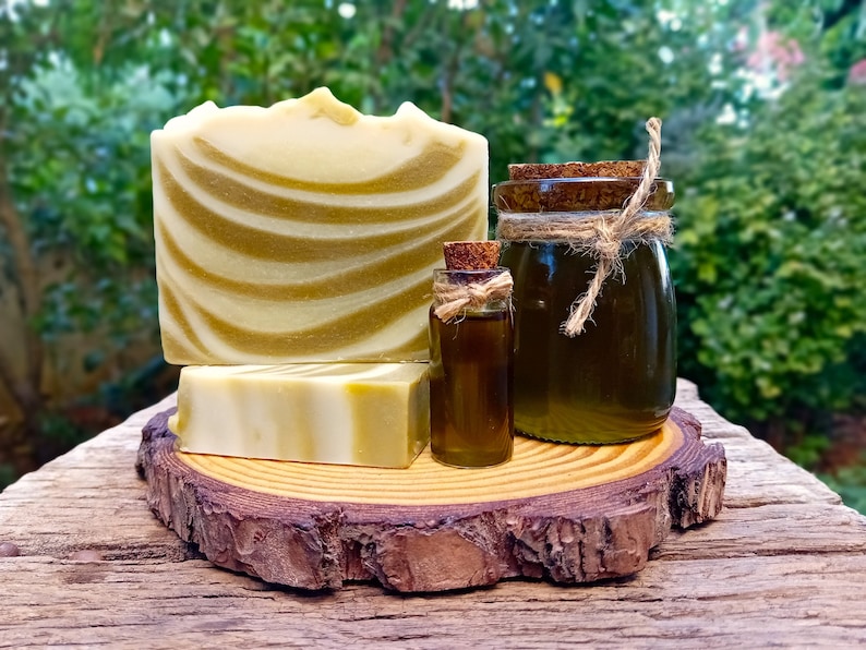 Puede incluir: Dos barras de jab&oacute;n de espiral verde y blanco y dos botellas de vidrio de l&iacute;quido verde con tapones de corcho sobre una rodaja de madera.