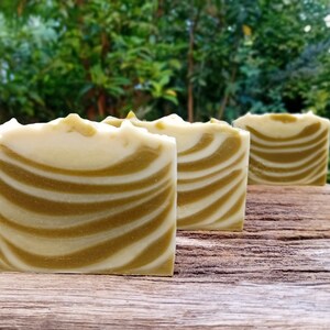 Puede incluir: Tres barras de jab&oacute;n artesanal con un patr&oacute;n de remolino blanco y verde. El jab&oacute;n est&aacute; dispuesto en una fila sobre una superficie de madera.